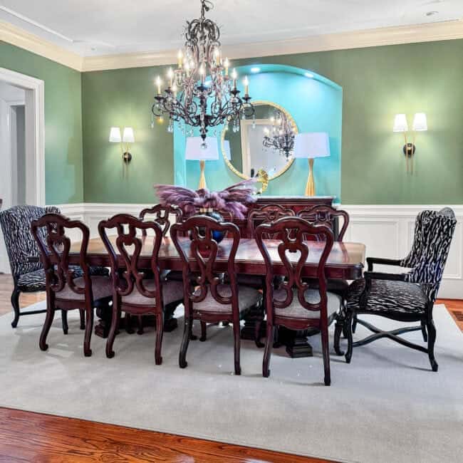 Cozy family dining with vintage wooden table, upholstered chairs, chandelier, modern wall lights, and colorful decor.