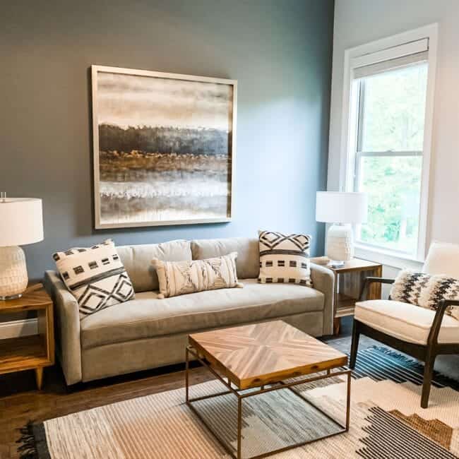 Bright living space with stylish sofa, decorative pillows, lamps, and contemporary artwork on a muted wall, creating welcoming ambiance.