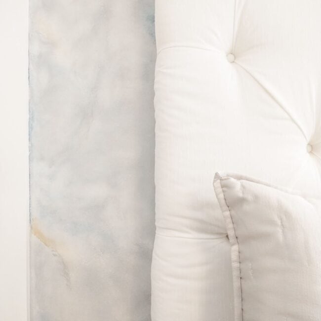 Luxurious white upholstered headboard with soft cushions against a contemporary wall art background.