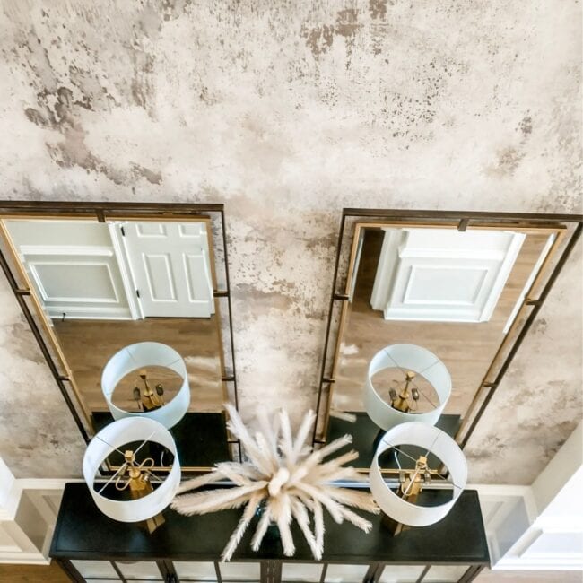 Elegant dining room with textured wall and farmhouse mirrors, featuring modern chandelier and stylish decor by DM Interiors.