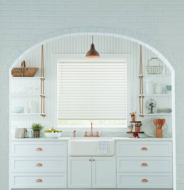 Bright white kitchen with open shelves, copper accents, and natural light from large window.
