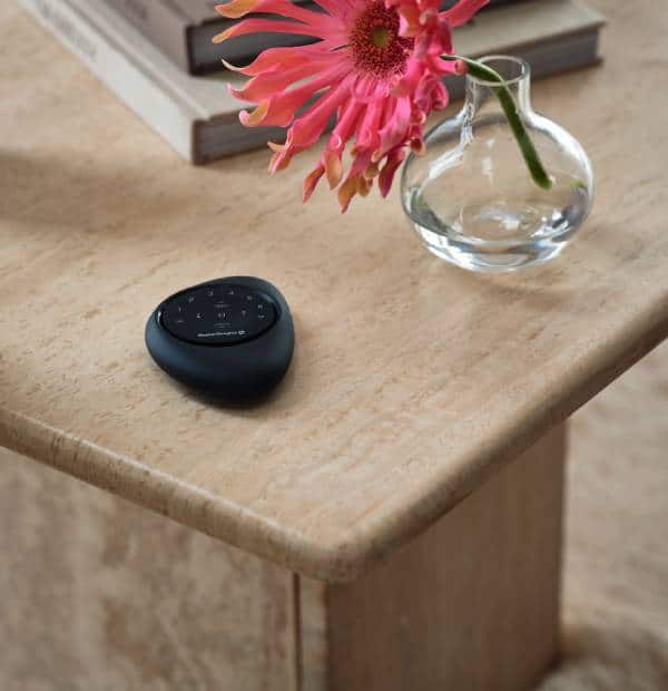 Smart speaker on wooden table with flower in glass vase and books, cozy home decor scene.
