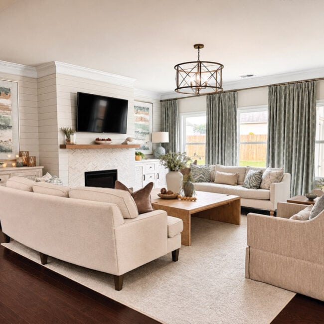 Spacious living room with beige sofas, fireplace, and large windows with green curtains.