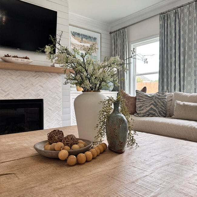 Living room with fireplace, floral arrangements, and large windows.