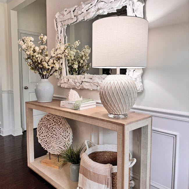 Decorative console table with lamp, mirror, and floral arrangement in entryway.