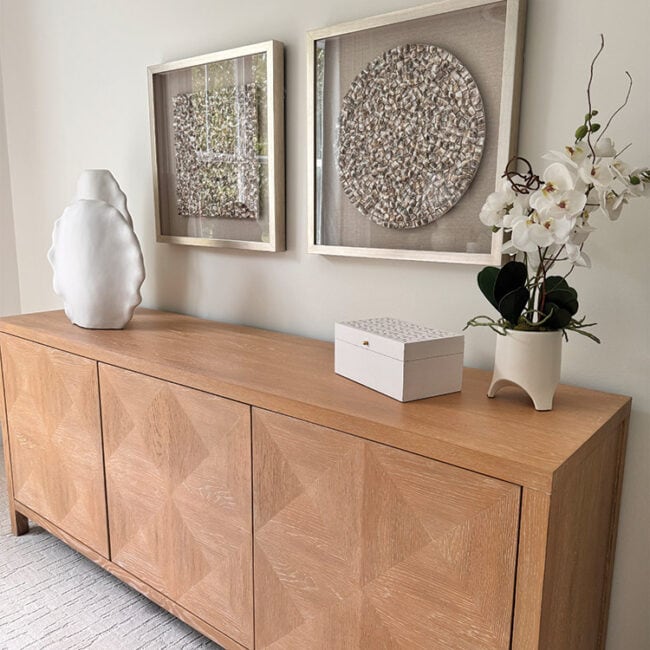 Wooden sideboard with white vase, orchid, and framed art.