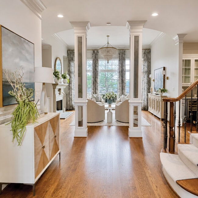 Bright living room with large windows, white furniture, and hardwood floors.