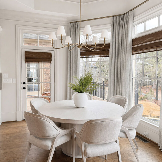 Bright dining room with round table, white chairs, and large windows with curtains.