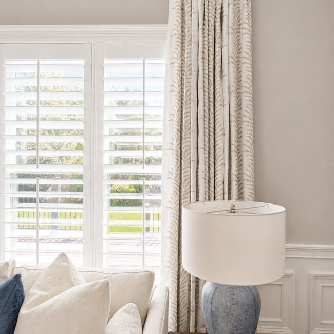 Living room with large windows, white curtains, and a beige sofa.