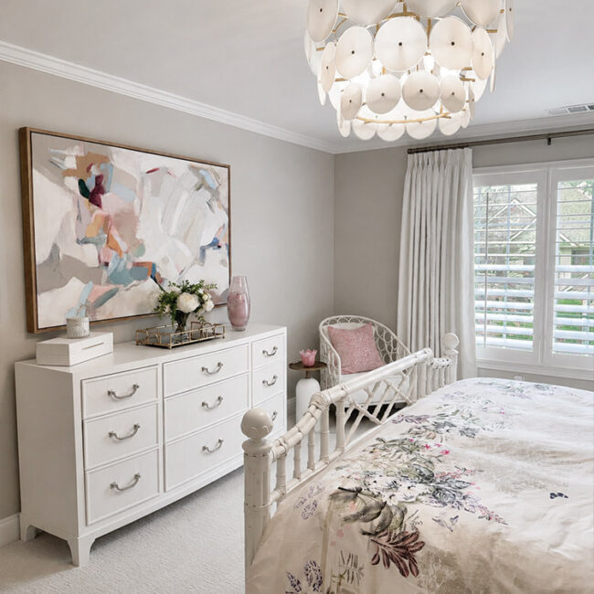 Cozy bedroom with white furniture, floral bedding, and modern chandelier.