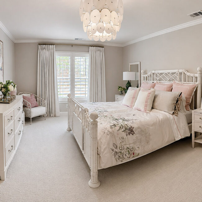 Bright bedroom with white furniture, floral bedding, and large window with curtains.