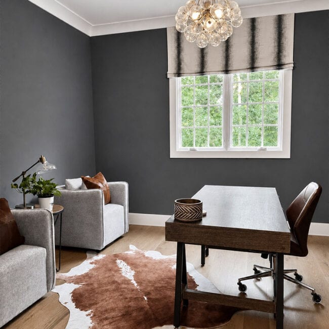 Stylish home office with dark gray walls, wooden desk, and large window with view of greenery.