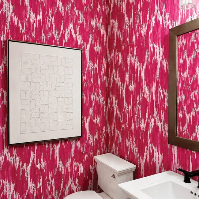 Bright pink and white patterned bathroom wall with mirror and artwork.