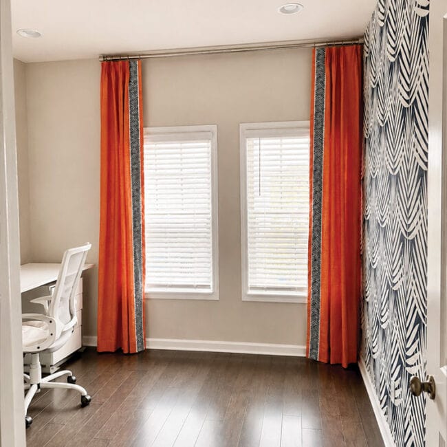 Home office with two windows, orange and patterned curtains, and a white desk and chair.