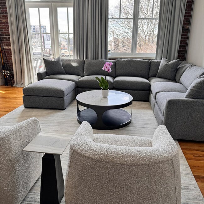 Bright living room with gray sectional sofa and large windows with curtains.