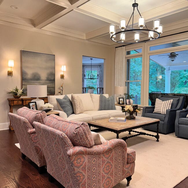 Spacious living room with comfortable sofas, chandelier, and large windows overlooking a garden.