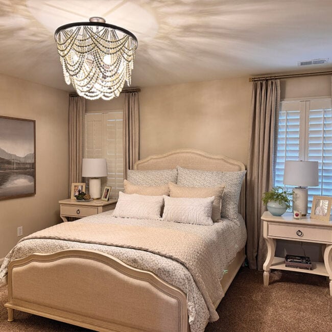 Cozy bedroom with beige walls, elegant chandelier, and matching nightstands.